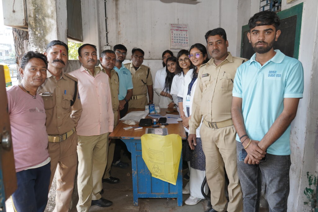 A group of people, including police officers in uniform and medical/volunteer staff, gathered around a wooden table indoors.