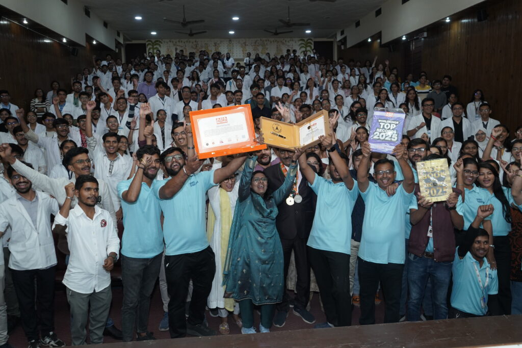 A large group of medical students and healthcare volunteers gathered in an auditorium, some holding awards and certification boxes, celebrating a record achievement during a Defeat Diabetese awareness event.